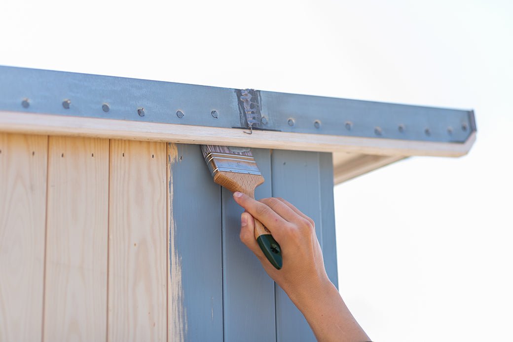 Hand painting a wooden surface with a brush, on a beach cabin.